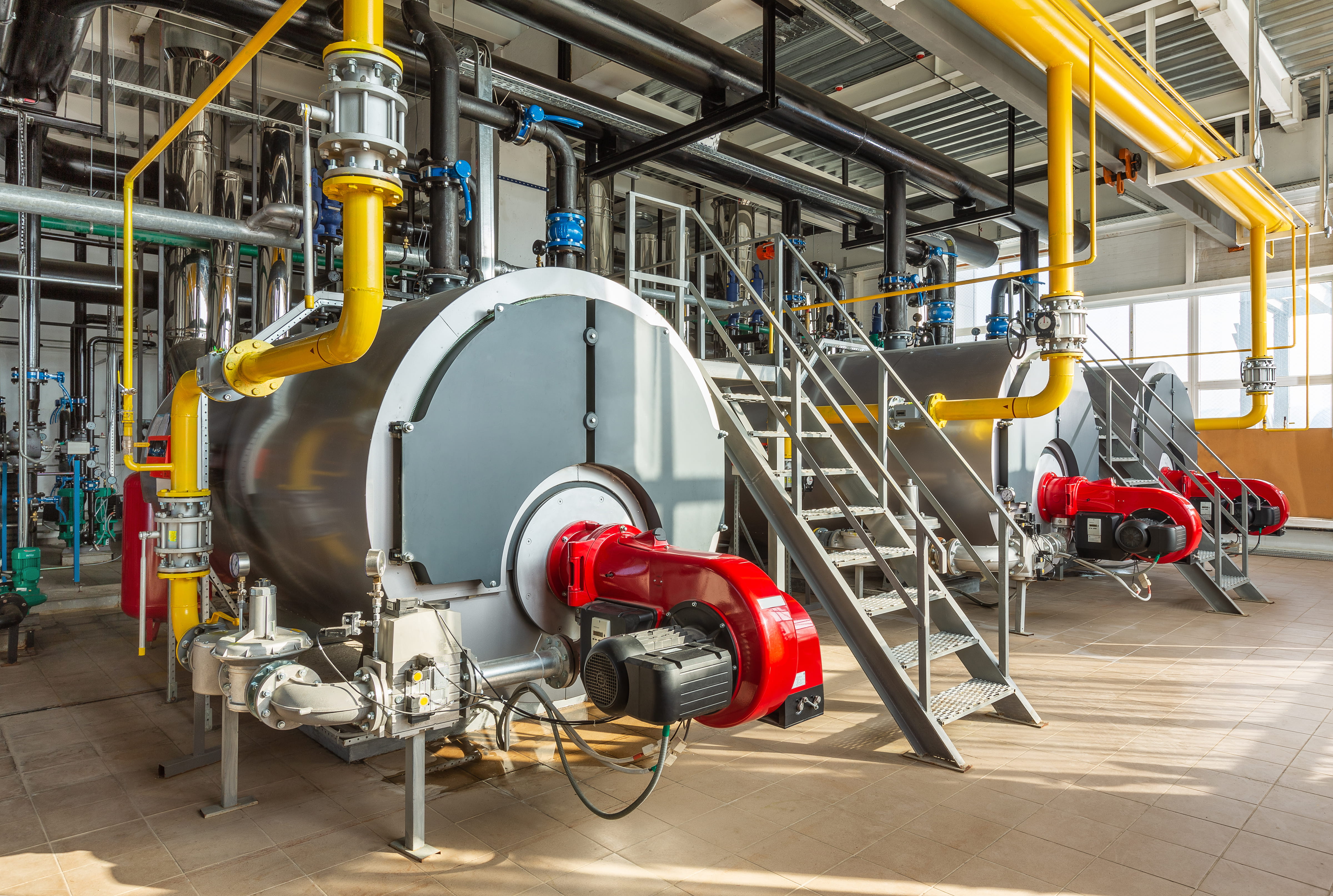 The interior of an industrial boiler room with three large boilers many pipes valves and sensors